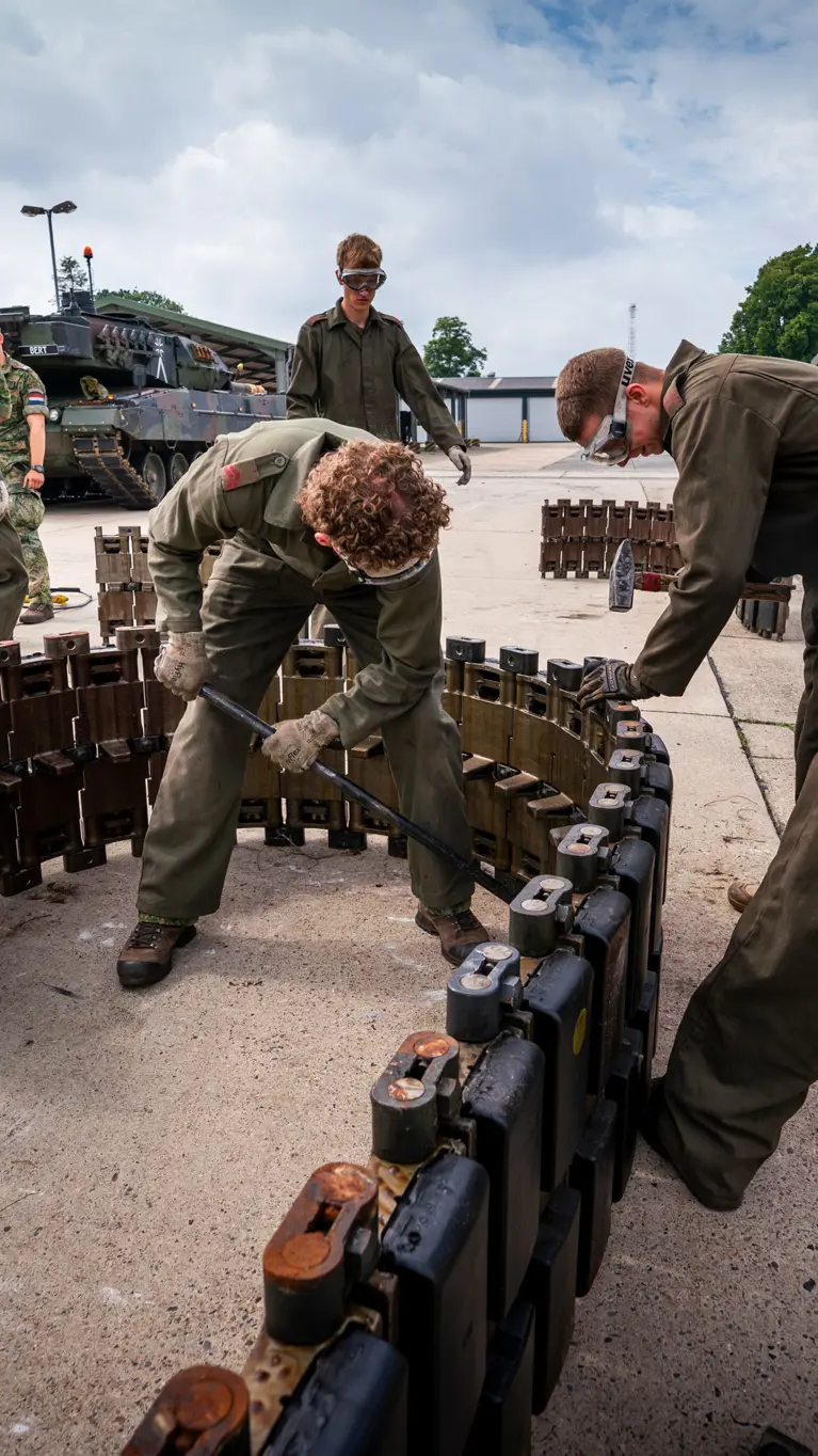 Een groep soldaten in groene overall werkt samen aan het monteren van een zware, metalen structuur in een buitenomgeving.
