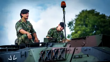 Twee cavaleristen met zwarte baret op zitten boven op de tank.