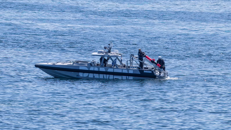 Kleine boot ligt stil op het water; aan de achterkant hangt een ronde onderwaterdrone.