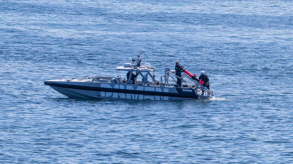 Kleine boot ligt stil op het water; aan de achterkant hangt een ronde onderwaterdrone.