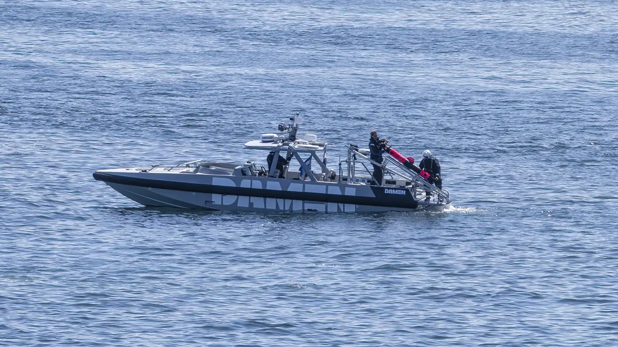 Kleine boot ligt stil op het water; aan de achterkant hangt een ronde onderwaterdrone.