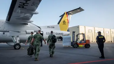 Op de eerste foto lopen militairen naar het witgele toestel. Rechts in beeld staat een vorkheftruck met een pallet vol flesjes water. 