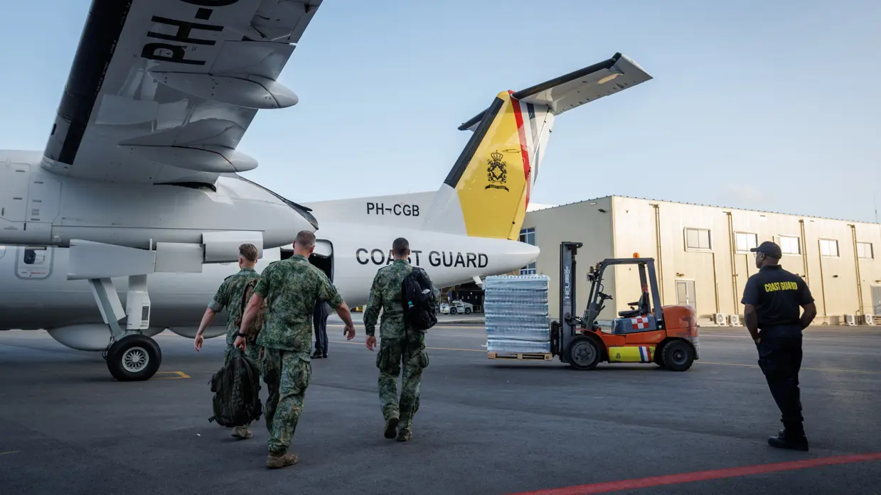 Op de eerste foto lopen militairen naar het witgele toestel. Rechts in beeld staat een vorkheftruck met een pallet vol flesjes water. 