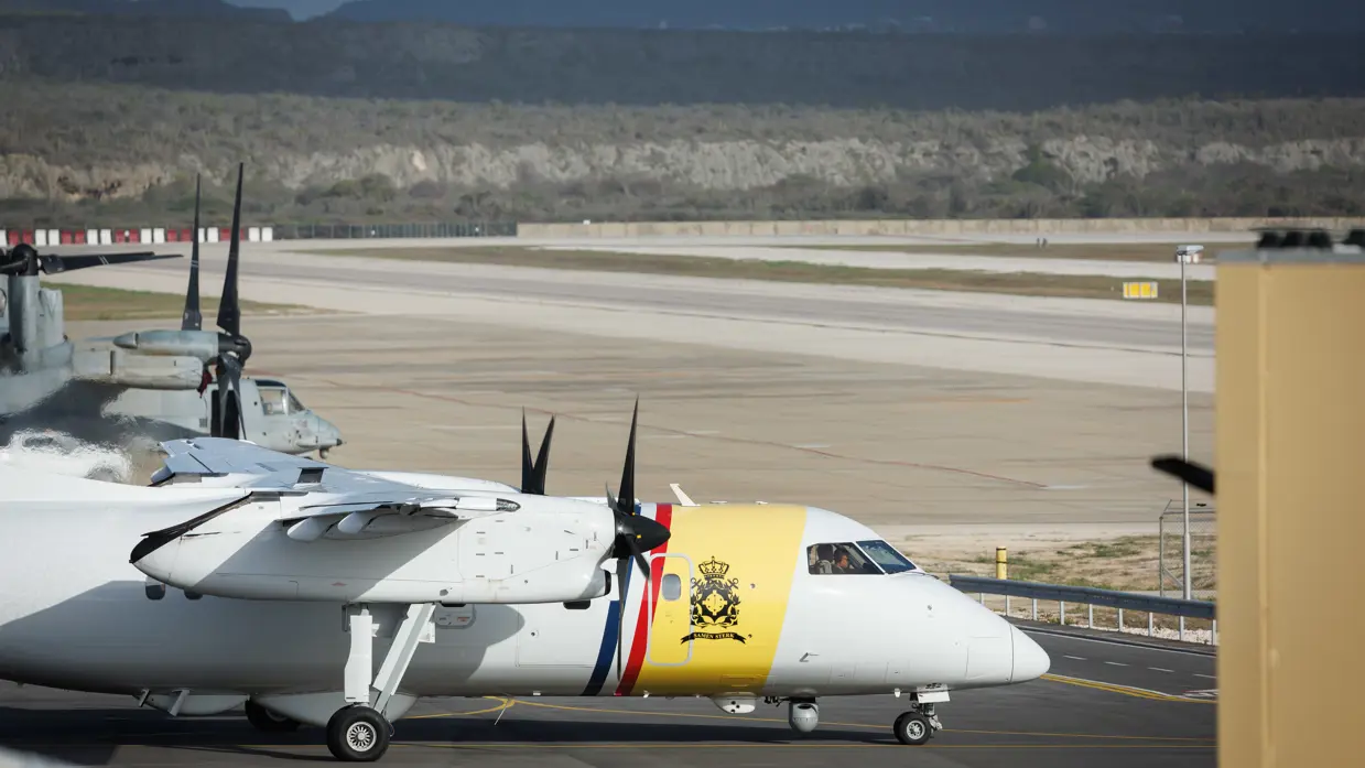 Op de tweede foto de witgele neus van het Dash 8 patrouillevliegtuig met daarachter een neus van een grijs vliegtuig.