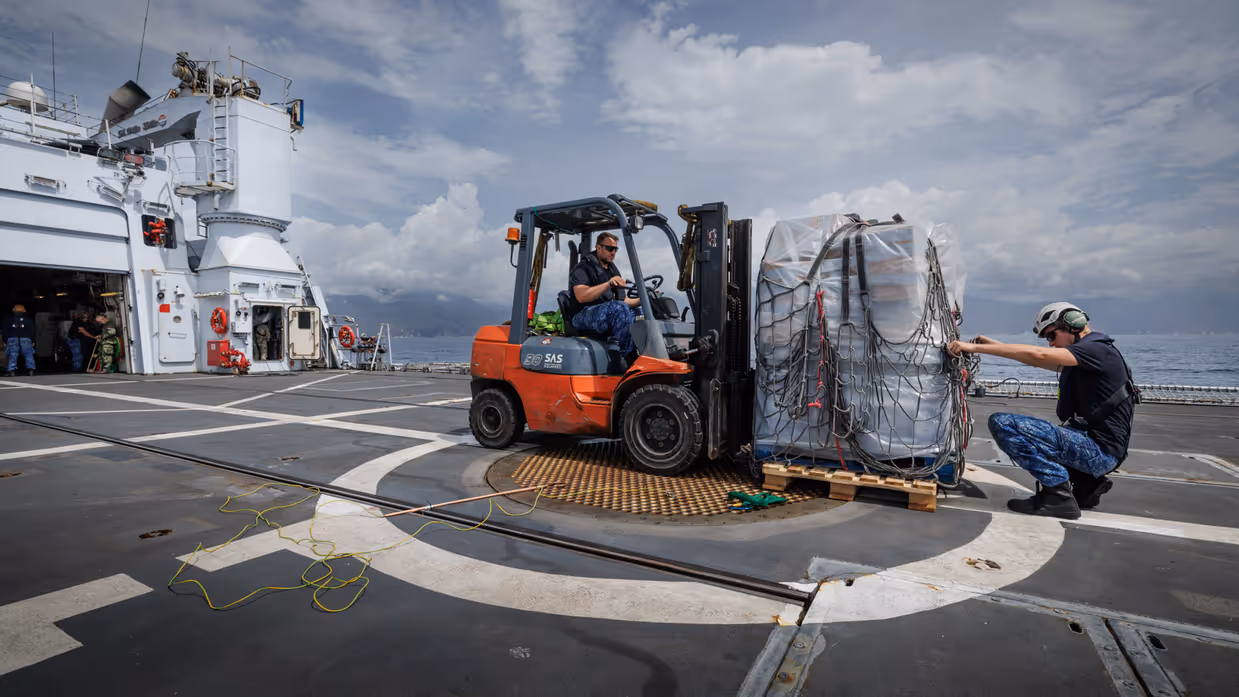 Een voorheftruck op het achterdek zet een pallet met waterflessen neer.