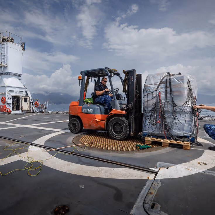 Een voorheftruck op het achterdek zet een pallet met waterflessen neer.