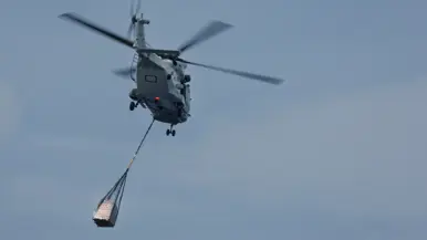 Op de eerste foto staat een pallet van boven gezien op het strand, ook is de schaduw van de helikopter te zien.