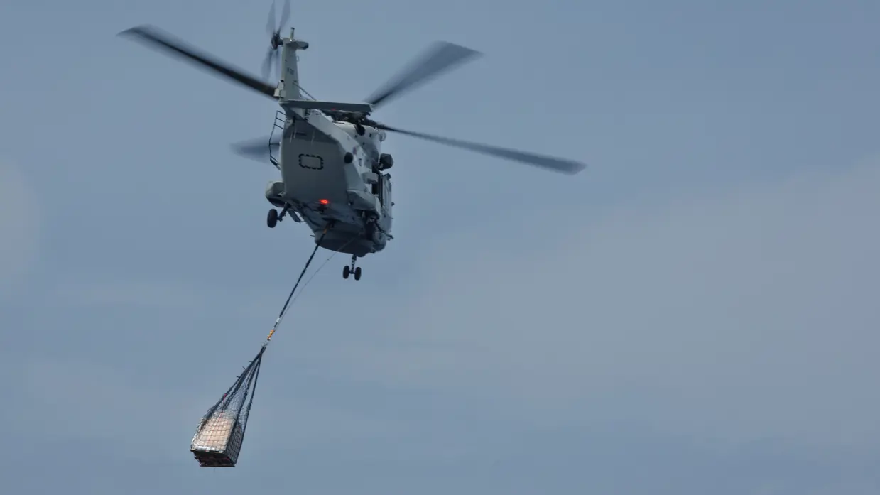 Op de eerste foto staat een pallet van boven gezien op het strand, ook is de schaduw van de helikopter te zien.