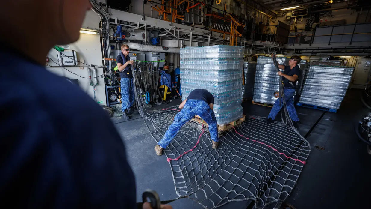 Op de rechter foto zijn militairen bezig een pallet hulpgoederen in te pakken in een groot, zwart bagagenet.