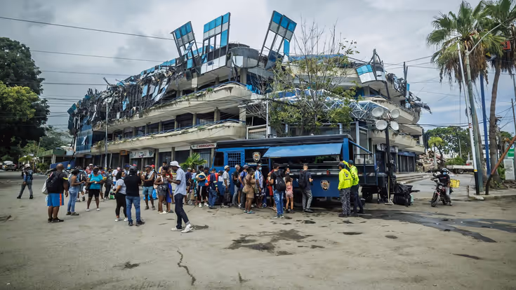 Een rij Venezolanen staat bij een hulppost, op de achtergrond een ingestort gebouw.