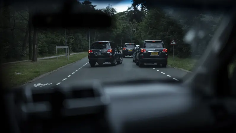 Drie antracietgrijze SUV’s sluiten een auto in op een bosrijke openbare weg.