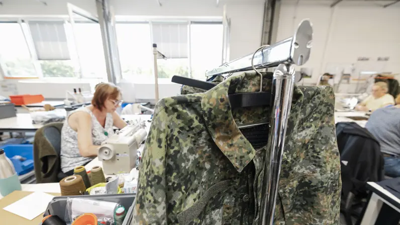 Militair kledingstuk hangt aan rek in atelier.