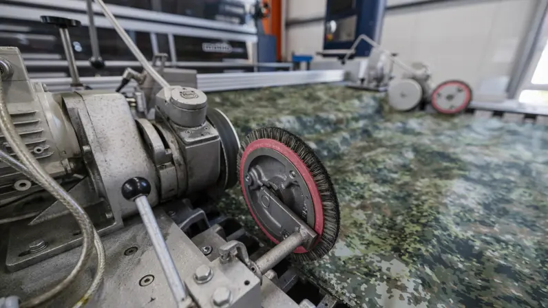 Stof met groen camouflagepatroon wordt door machine geleid tijdens controle op productiefouten.