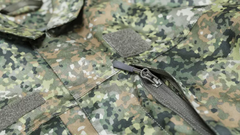 Detail van rits borstzak op militair pak in groen camouflagepatroon.