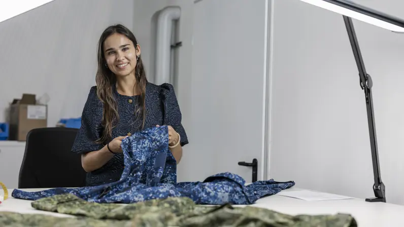 Vrouw achter werktafel controleert militaire uniformen.