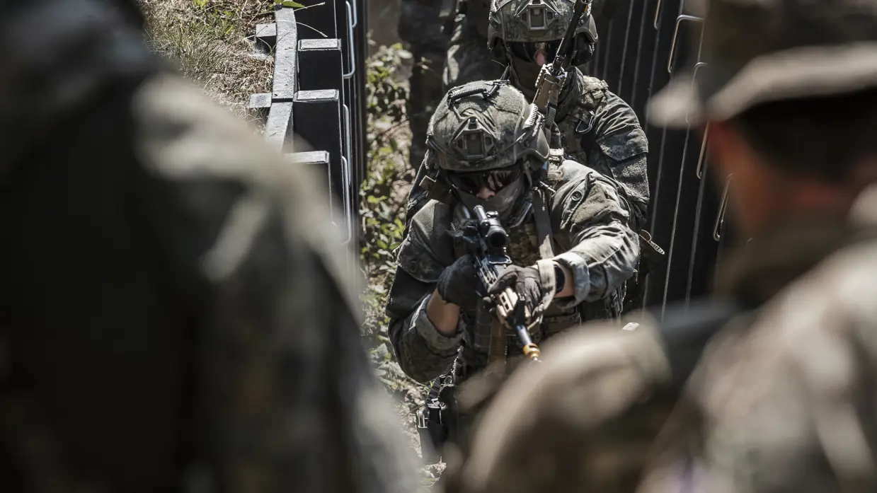Een groep studentmilitairen bewegen door een loopgraaf.