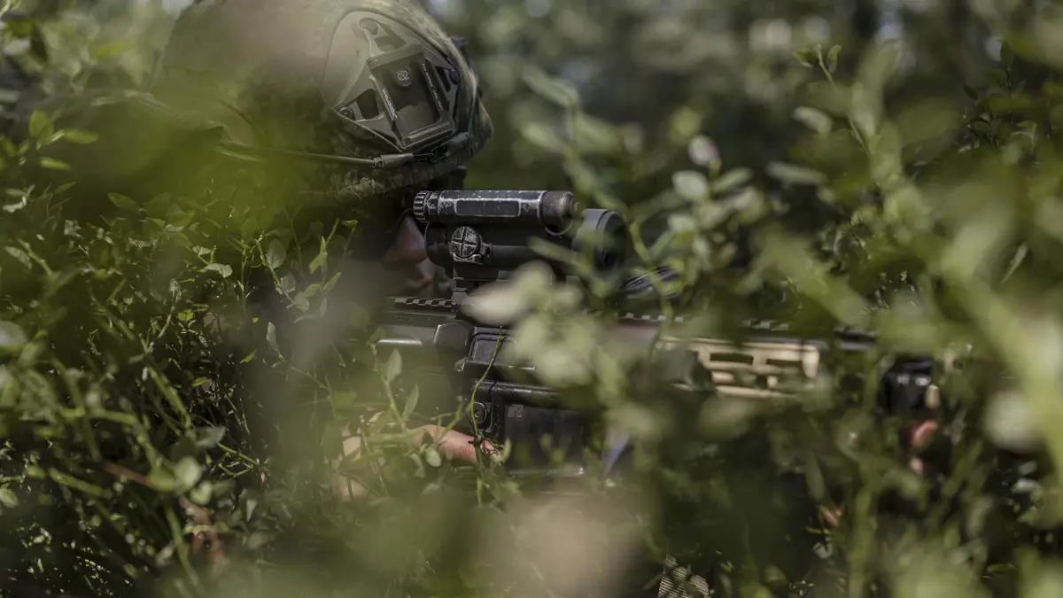 Een militair staat paraat met een geweer in de bosjes.