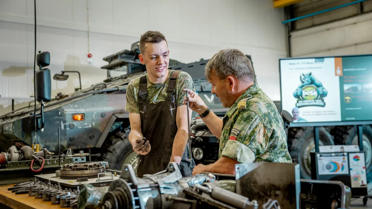 een monteur die aan een collega uitleg geeft over een voertuigmotor. 