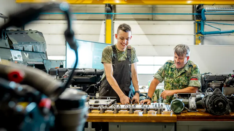 de sergeant-majoor een collega naar elkaar lachend bij een motor in de werkplaats. 