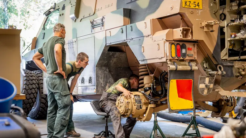 twee monteurs kijken hoe een collega aan de rem sleutelt van een groot wielvoertuig.