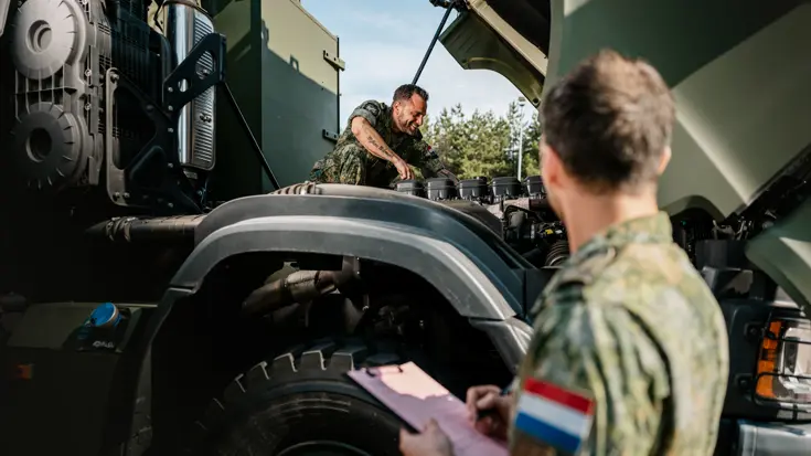Mike sleutelt aan een Scania terwijl een collega een lijst bijhoudt.