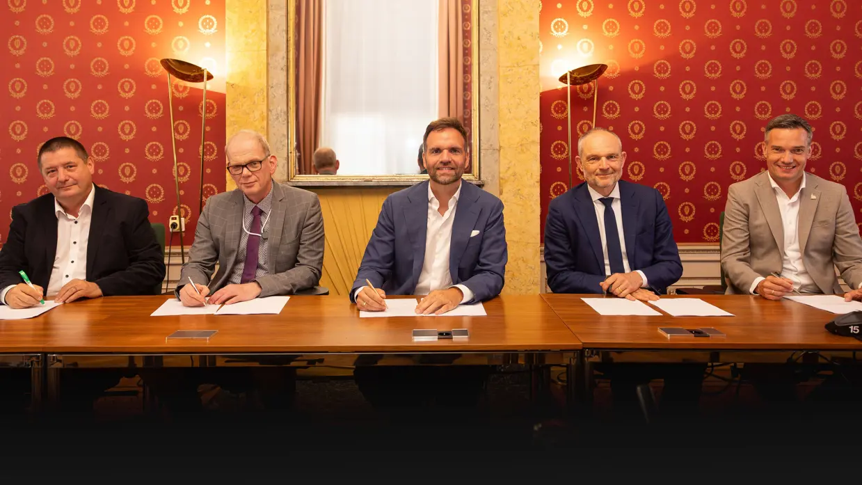 Vijf mannen aan een ondertekeningstafel naast elkaar. In het midden zit Boswijk.