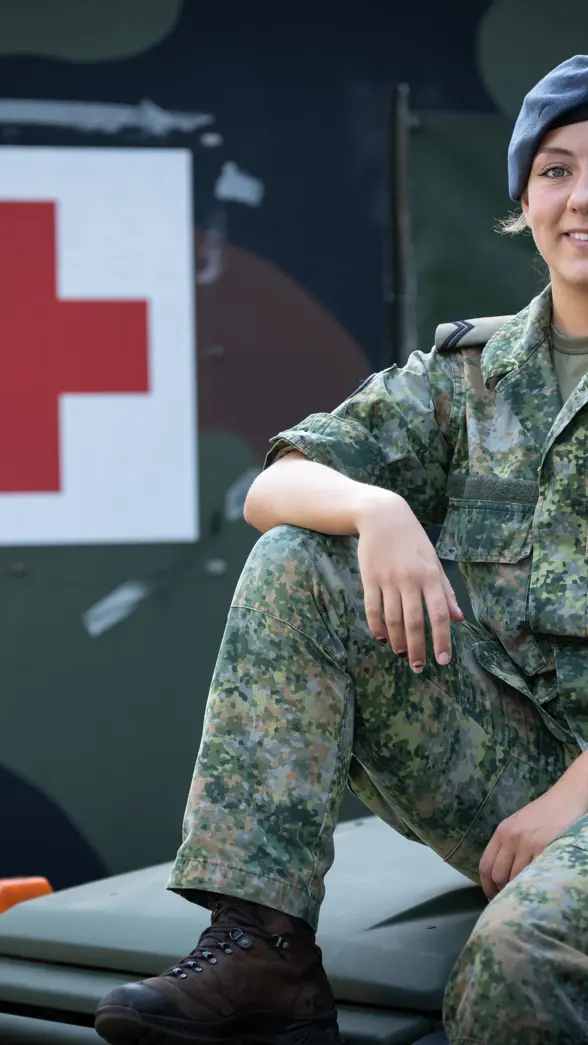 Militair in uniform zit op motorkap ambulance. Op de achtergrond een groot rood kruis op de zijkant van een andere ambulance.