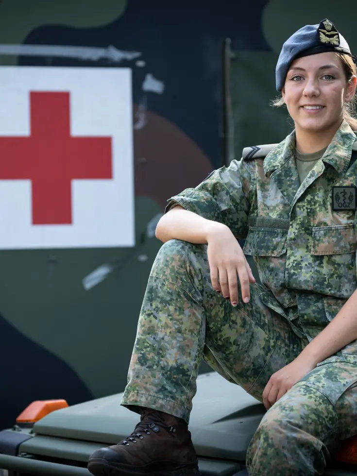 Militair in uniform zit op motorkap ambulance. Op de achtergrond een groot rood kruis op de zijkant van een andere ambulance.