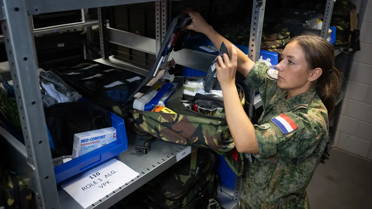 Militair controleert medische spullen in rugzak op plank van magazijn.