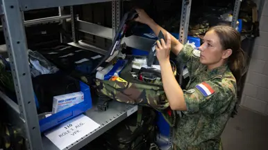 Militair controleert medische spullen in rugzak op plank van magazijn.