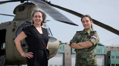 Militair en burgermedewerker staan voor Chinook. In de lucht in de achtergrond vliegt een NH90.