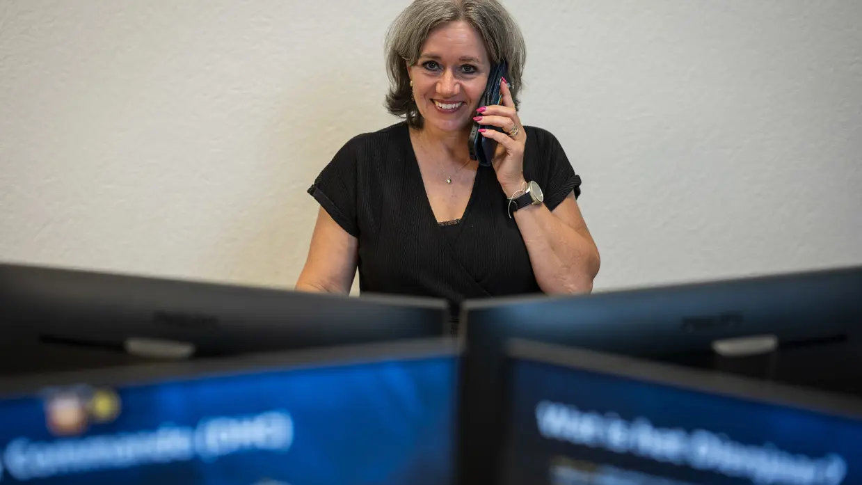 Vrouw zit bellend achter computerschermen op kantoor.
