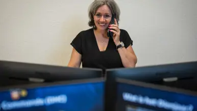 Vrouw zit bellend achter computerschermen op kantoor.