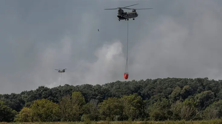 Een Chinook vliegt weg met een volle Baby Bucket boven een water.