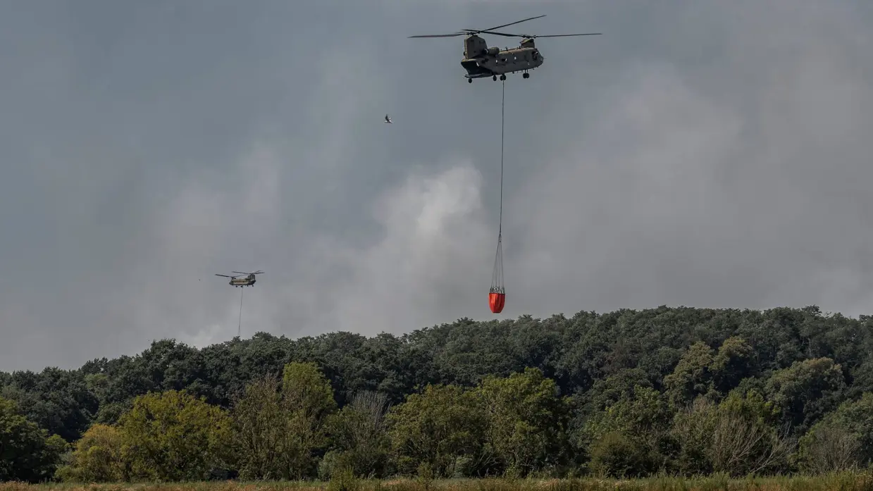 Een Chinook vliegt weg met een volle Baby Bucket boven een water.