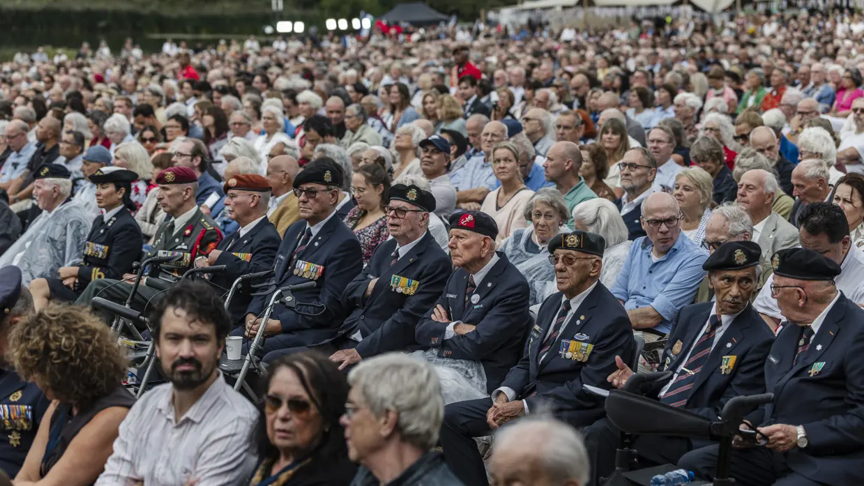 Honderden mensen zittend publiek met daartussen een rij veteranen op hoge leeftijd.