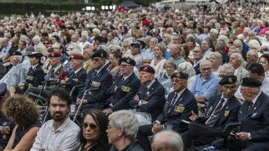 Honderden mensen zittend publiek met daartussen een rij veteranen op hoge leeftijd.