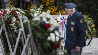 Een veteraan op leeftijd bekijkt de bloemenkransen op de standaarden van dichtbij.