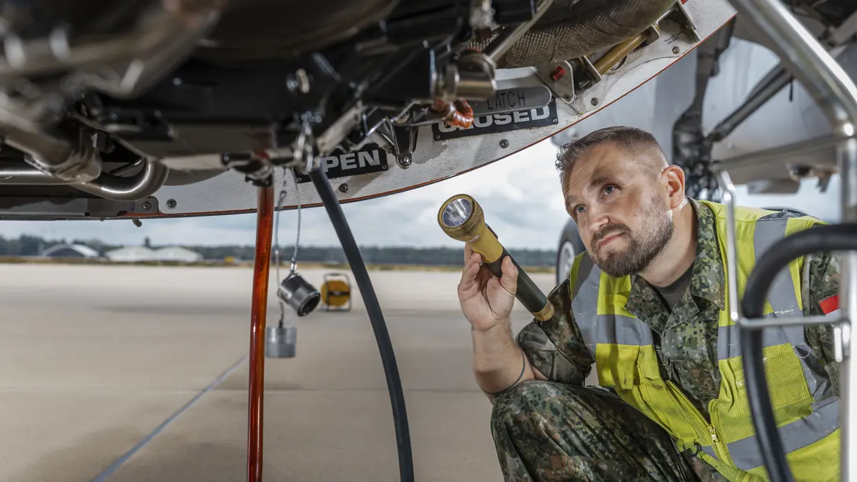 Roy van der Mark met geel hesje aan, schijnt met een zaklantaarn in mortorgondel van een A330 MRTT.