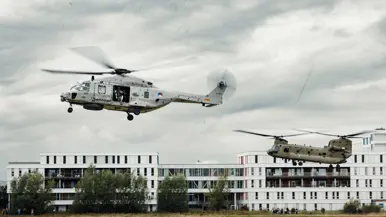 2 helikopters vliegen achter elkaar voor een ziekenhuis.