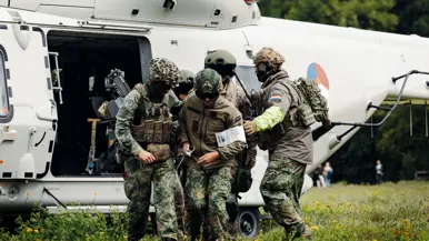 5 gecamoufleerde militairen rennen gegroepeerd uit een helikopter. 