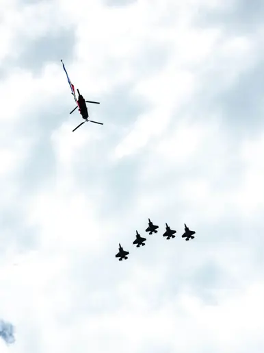 Van onderaf gezien: vijf vliegende F-35’s en een Chinook met daaronder een wapperende Nederlandse vlag.