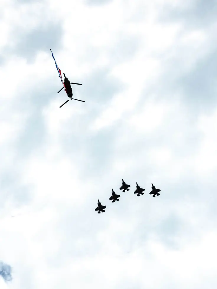 Van onderaf gezien: vijf vliegende F-35’s en een Chinook met daaronder een wapperende Nederlandse vlag.