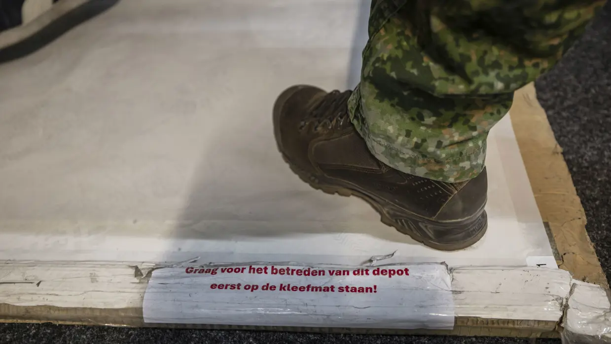 Iemand stapt op een kleefmat met daarop de tekst: “Graag voor het betreden van dit depot eerst op de kleefmat staan!”