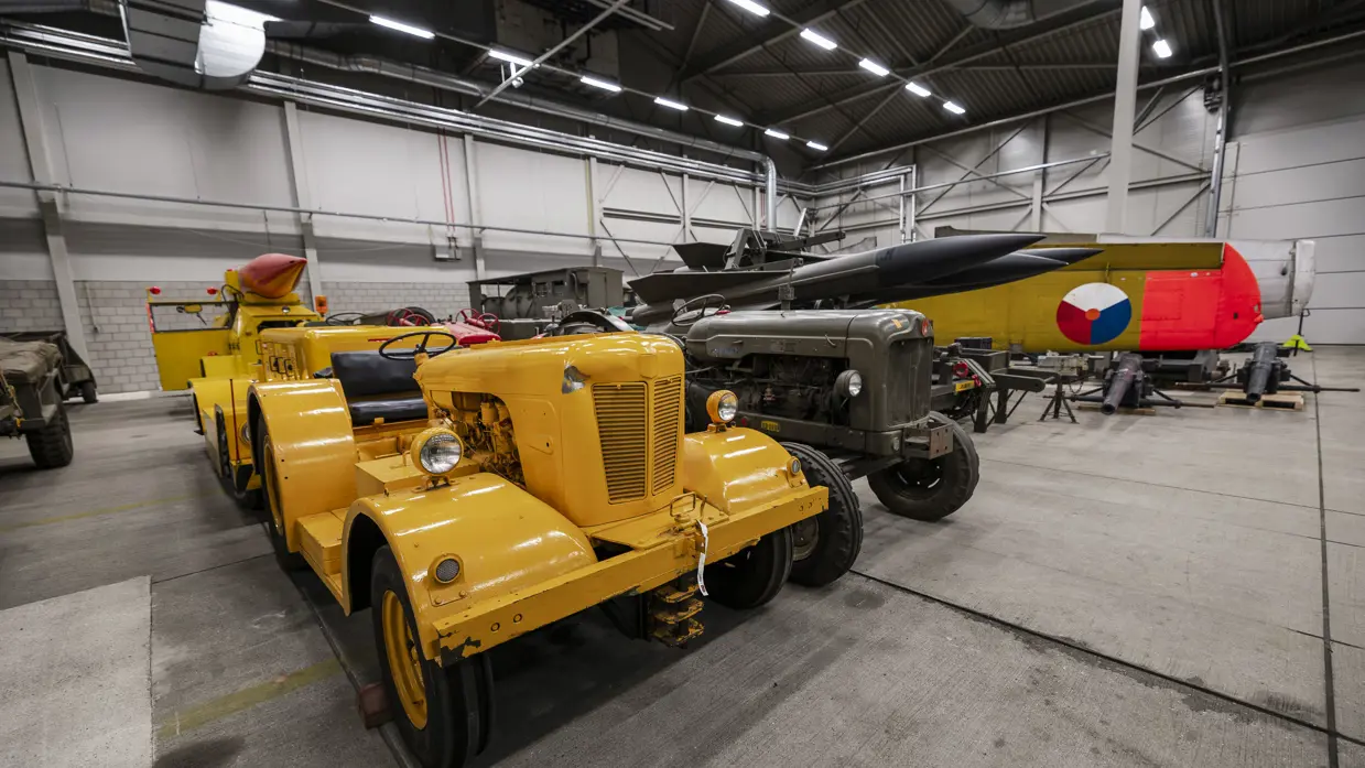 Een knalgeel voertuig staat naast een groene tractor, erachter de raketten van het HAWK-wapensysteem.