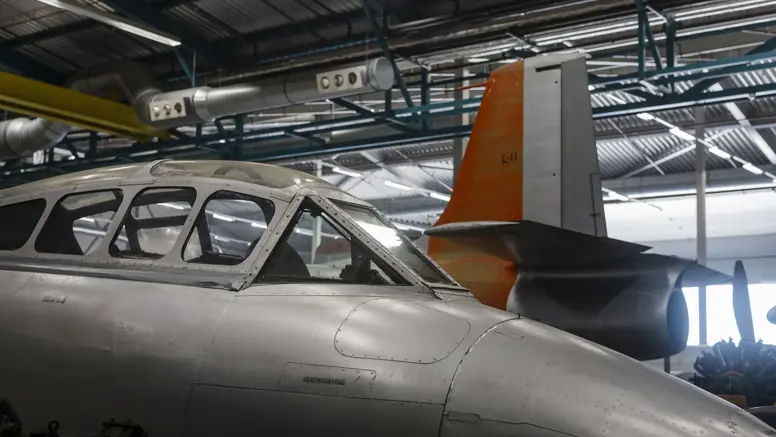 Close-up van een cockpit van een oud jachtvliegtuig met daarachter het staartstuk van een ander toestel.