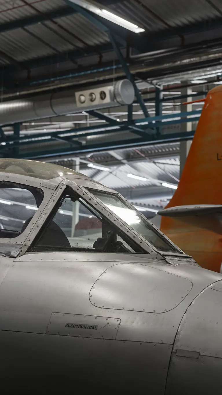 Close-up van een cockpit van een oud jachtvliegtuig met daarachter het staartstuk van een ander toestel.