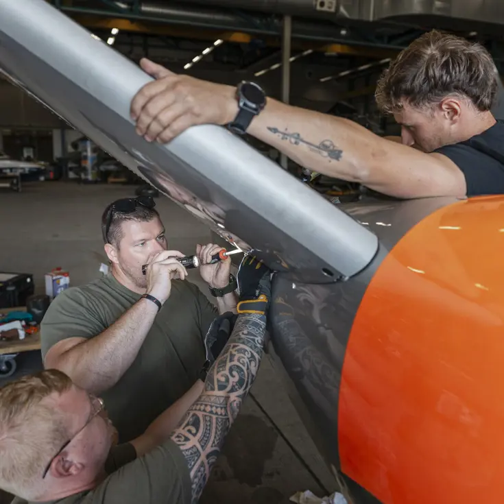 Drie militairen sleutelen aan het staartstuk van een lesvliegtuig.