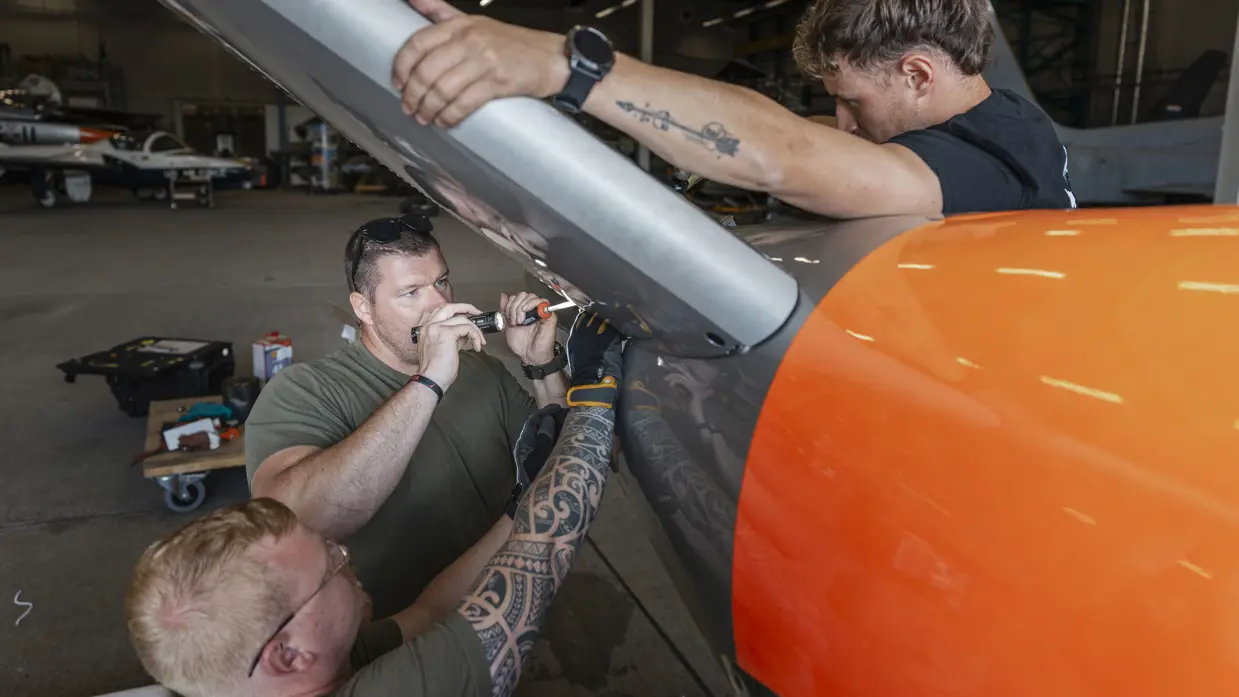 Drie militairen sleutelen aan het staartstuk van een lesvliegtuig.