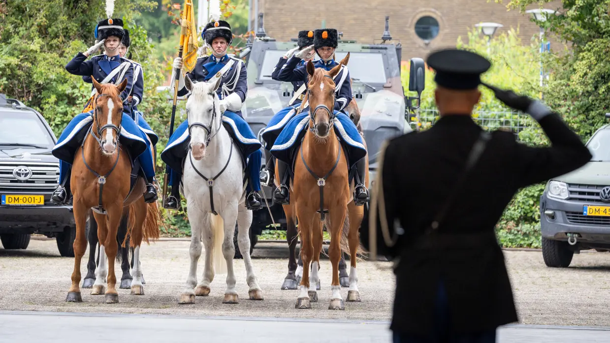 C-KMar Costongs van op de rug bezien, salueert naar ruiters te paard die teruggroeten.